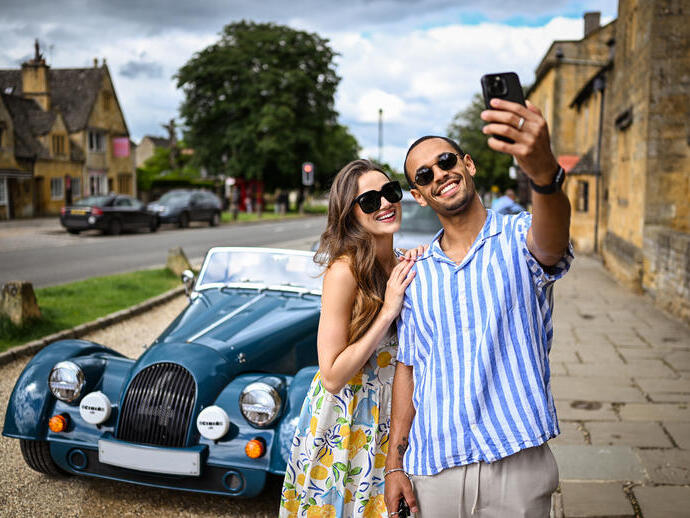 A man and a woman take a selfie in front of a classic car