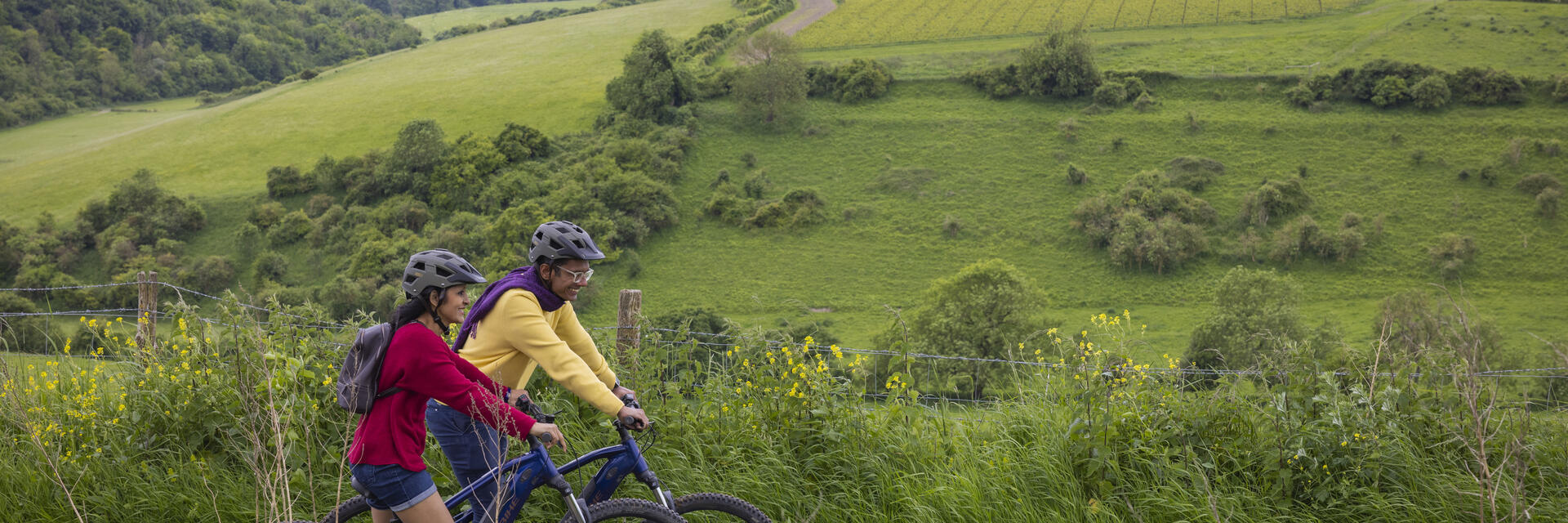 A man and a woman stand with bicycles wearing helmets