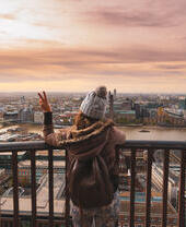 Woman on a balcony at the top of a high building looking over a city