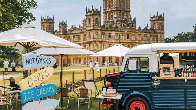 A food truck, parasols and direction signs in the ground of a castle