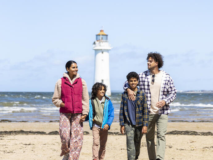Family walk along a beach with a lighthouse in the background