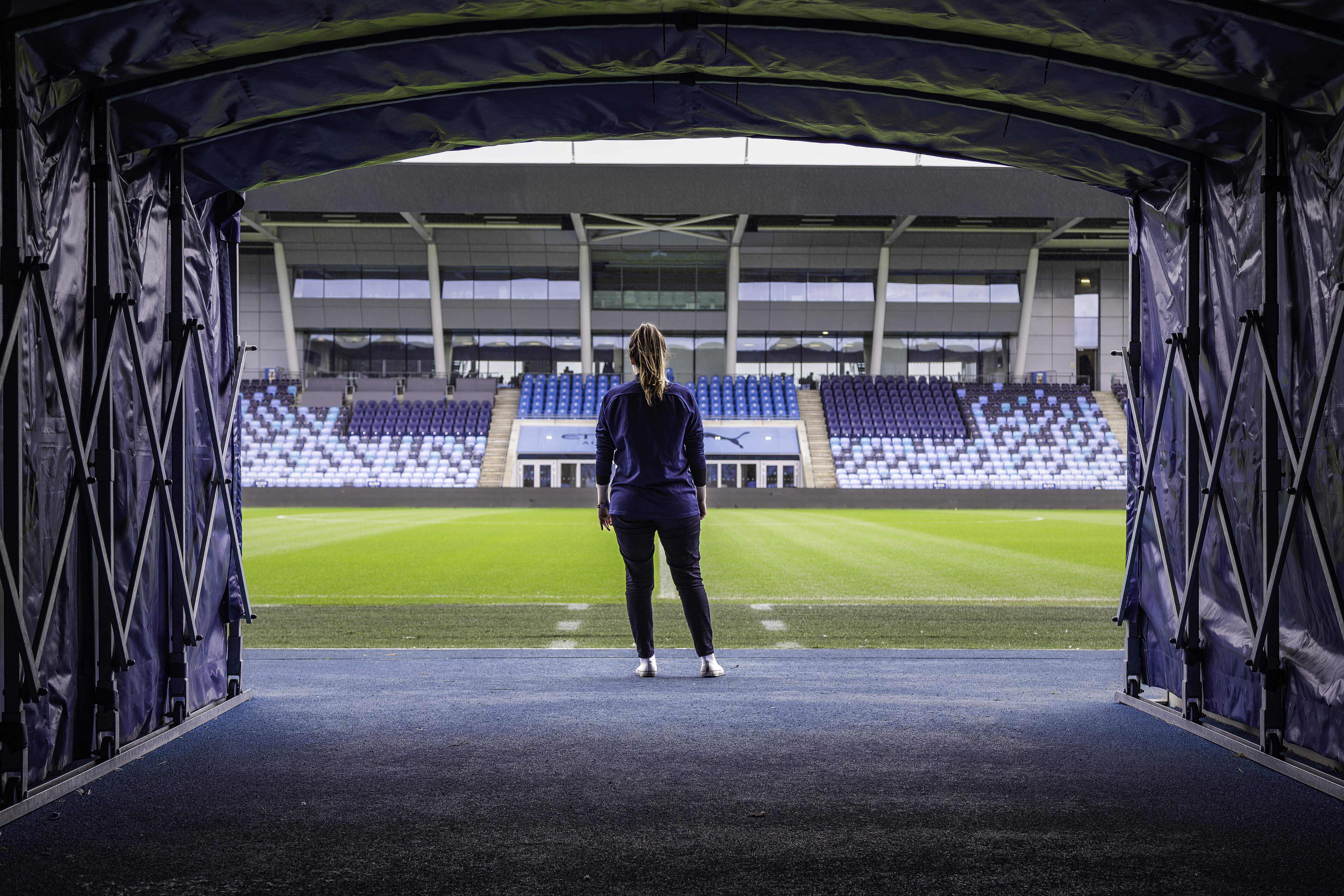 Mujer de pie frente al campo del estadio de la Academia del Manchester City.