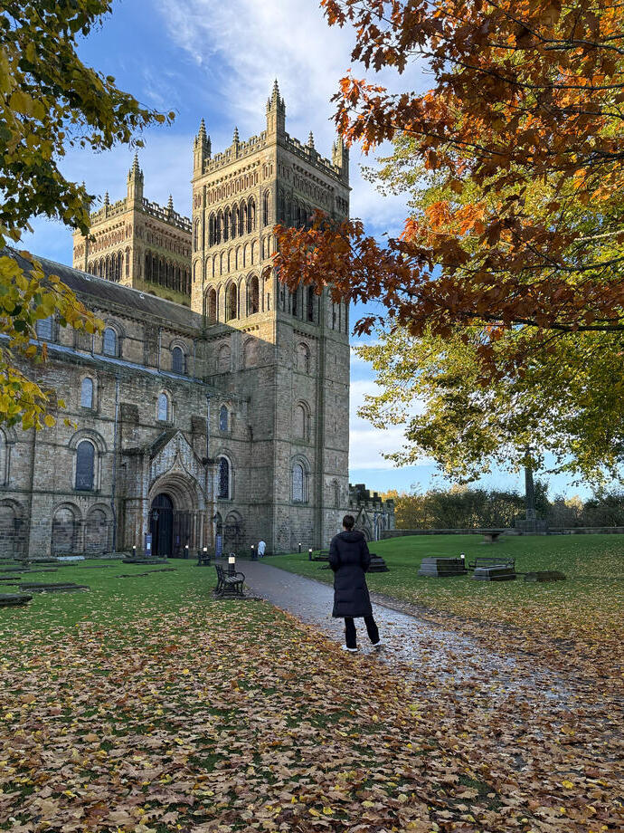 A woman in a warm jacket facing a large cathedral and tower.