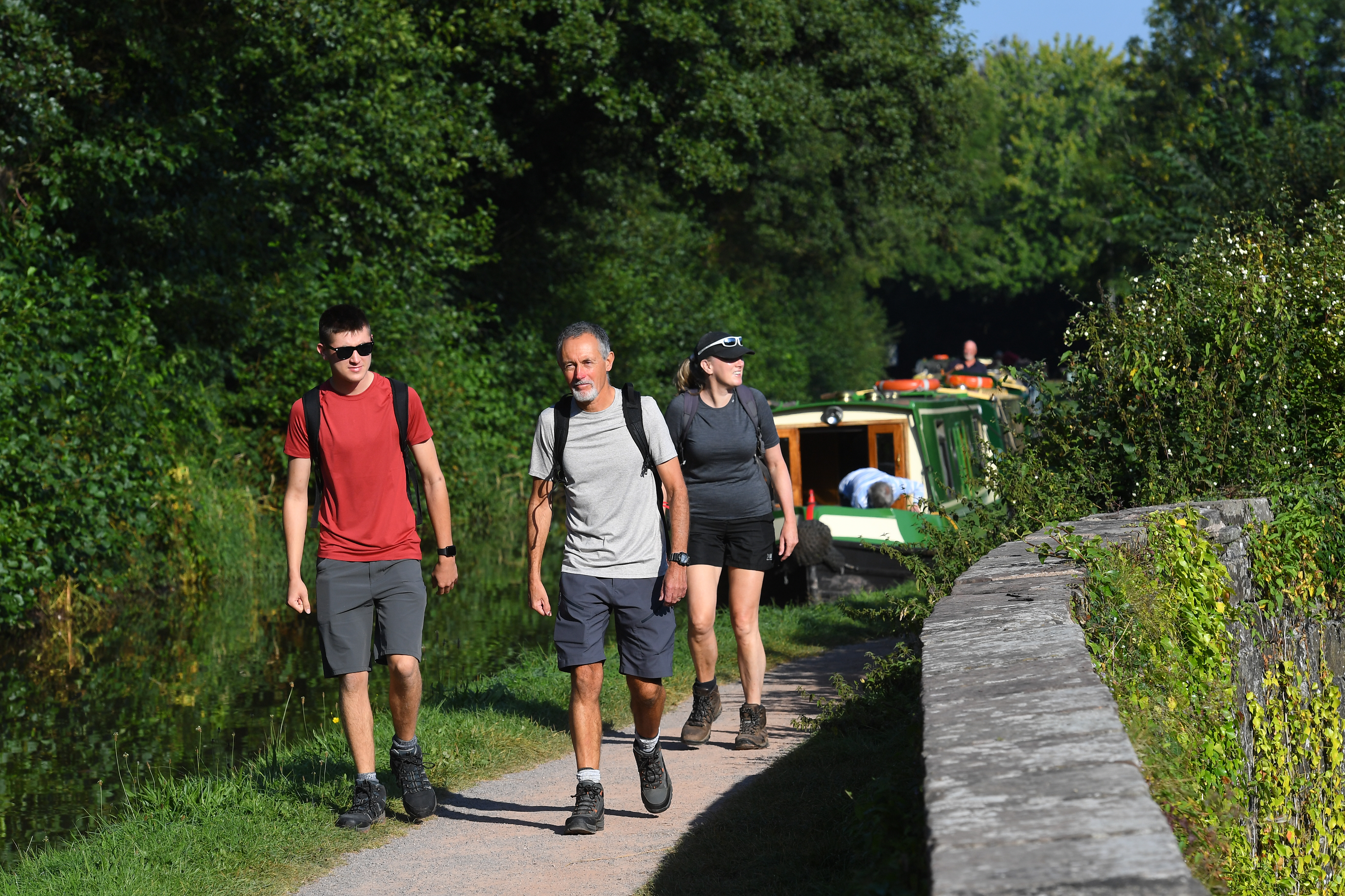 Trois personnes marchant sur un chemin le long d'un canal où sont amarrés des bateaux.