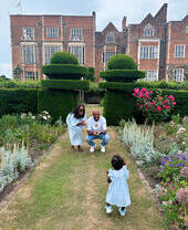 Man, woman and child playing in formal garden of large country house