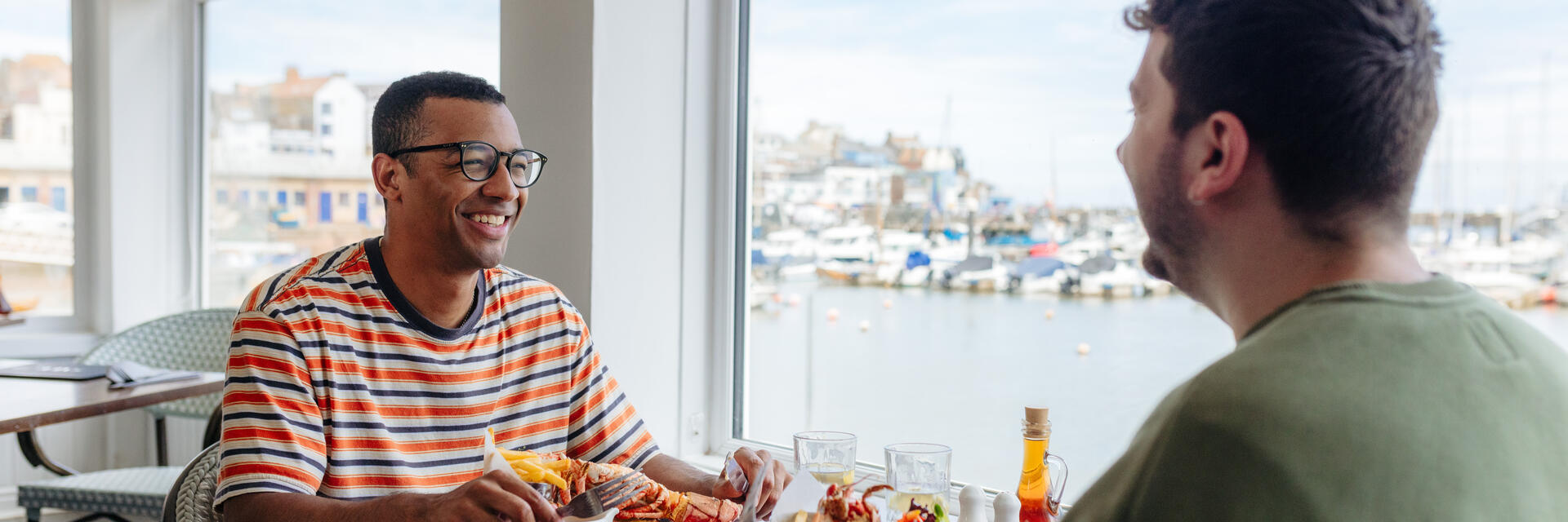 Two men eat lobster in a restaurant with a harbour view