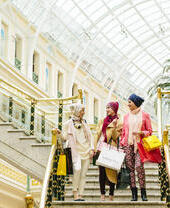 ثلاث نساء يرتدين أوشحة، يمشين حاملات أكياس التسوق