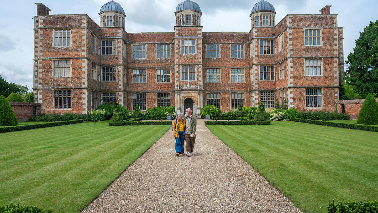 Ein Mann und eine Frau spazieren gemeinsam auf einem Weg vor einem historischen Gebäude