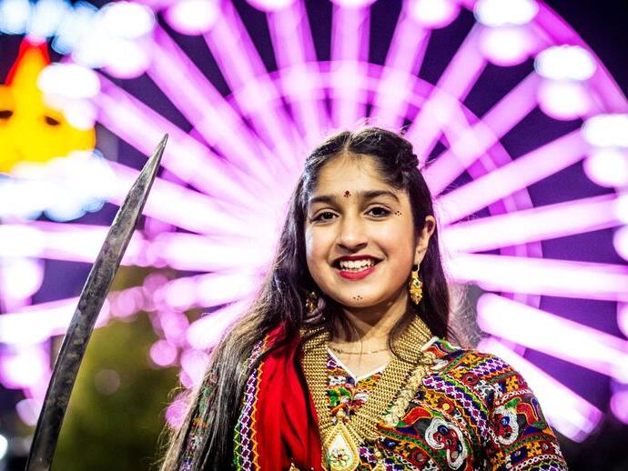 A woman celebrating Divali in front of a large lit up wheel