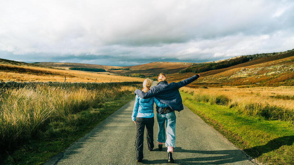 Rear view of two people walking down a countryside road