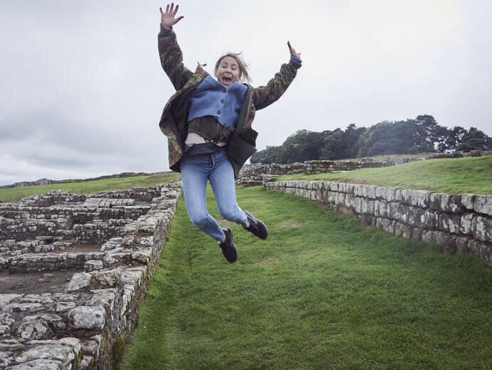 Girl leaping into the air with raised arms near stone wall