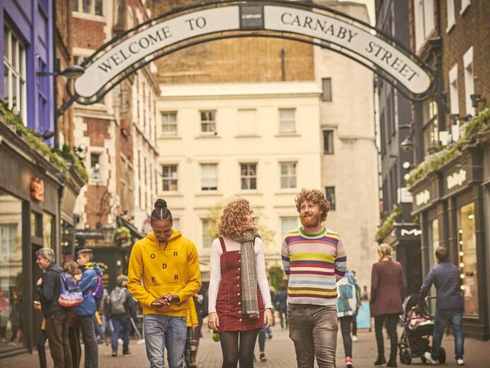 Una donna e due uomini che camminano lungo una via dello shopping
