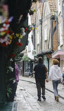 A man and a woman walk down a cobbled street holding hands