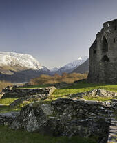Ruins of a castle in the countryside surrounded by mountains.