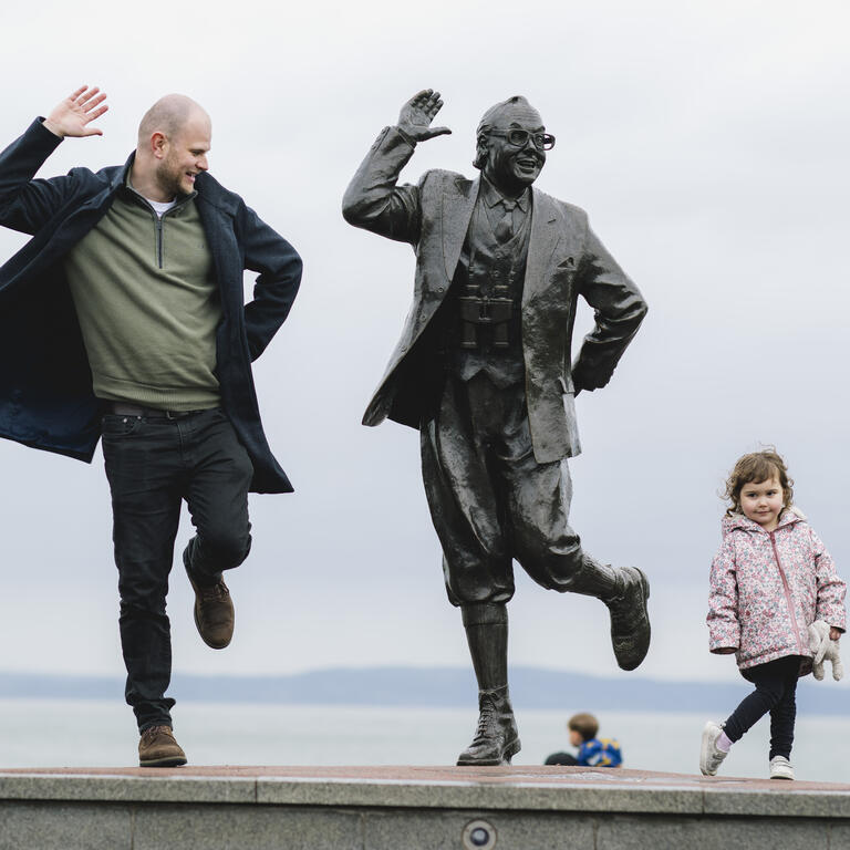 View of man, female child and statue of a man in front of the sea