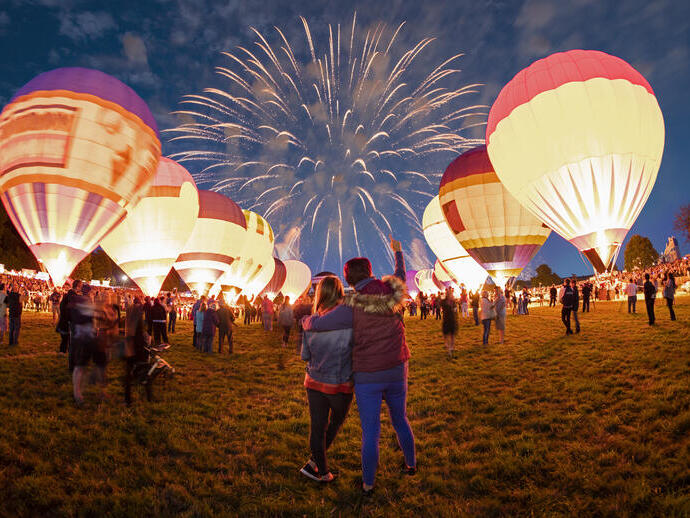 Couple regardant des montgolfières au sol et des feux d'artifice dans le ciel nocturne