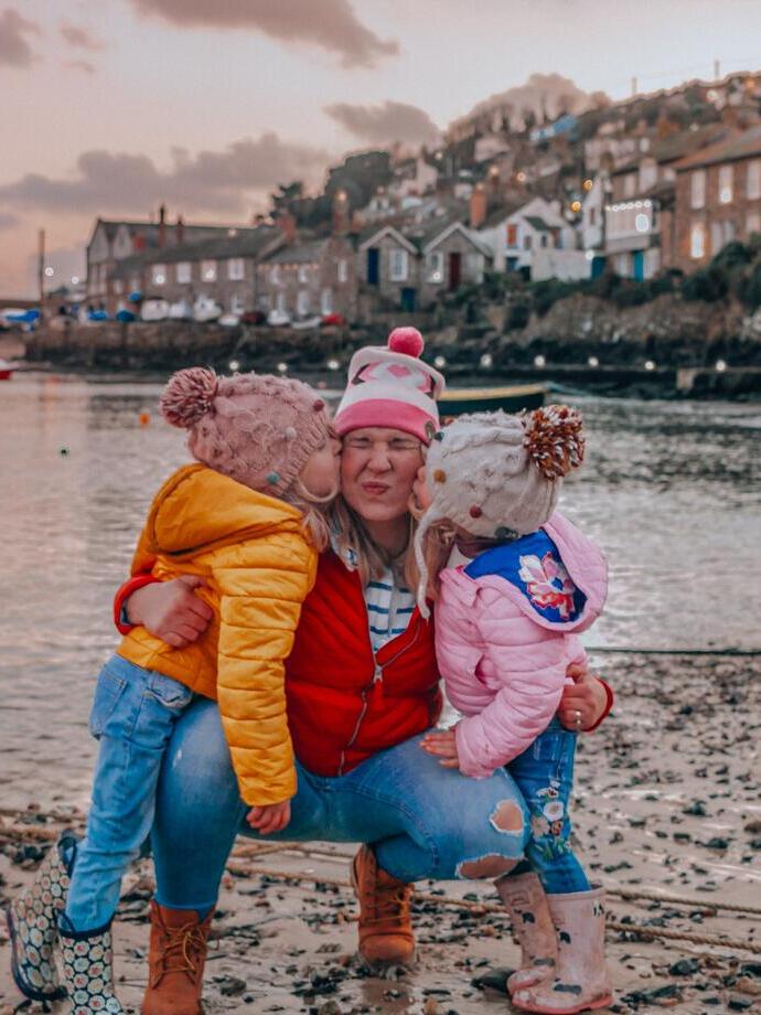 Two children giving a woman a kiss on the cheek on a beach