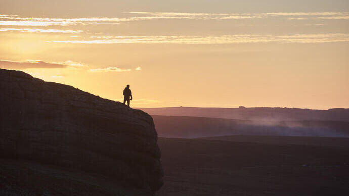 Silhouette einer Person, die bei Sonnenuntergang auf einem großen Hügel wandert