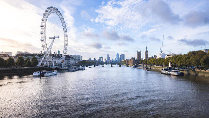 Blick auf einen Fluss und eine Brücke mit einem großen Riesenrad und berühmten Gebäuden im Hintergrund.