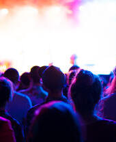 Public d'un concert applaudissant et regardant un spectacle sur scène.