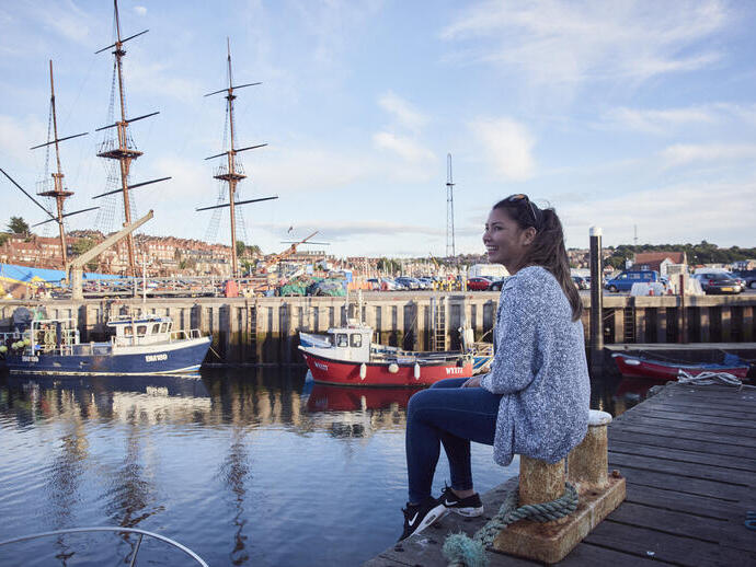 Lächelnde Frau, die auf einem Steg in einem Hafen sitzt