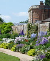 A walkway through a pretty walled garden blooming with flowers.