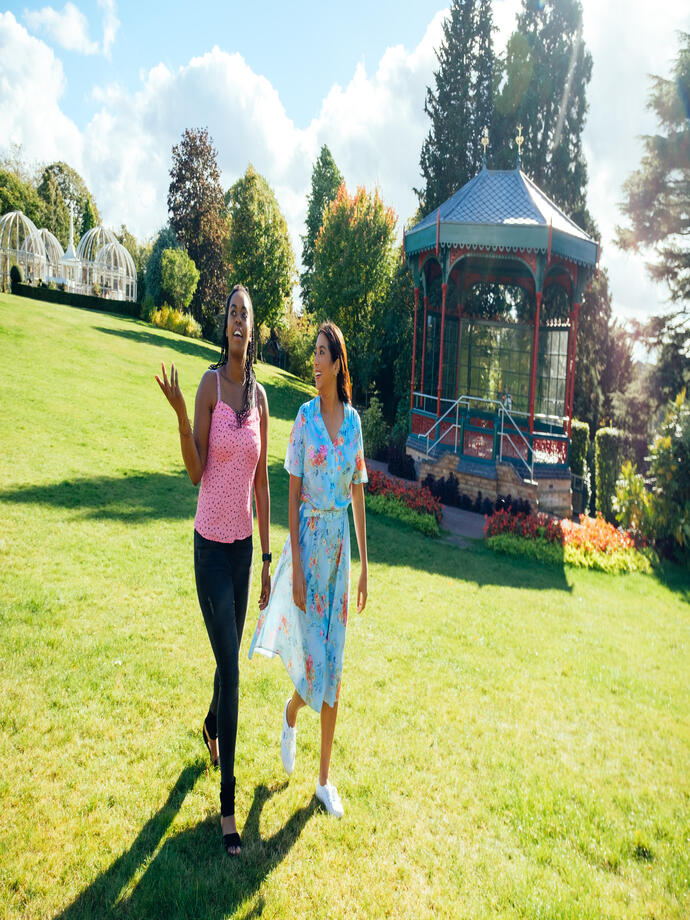 Two women walking on grass past a pergola