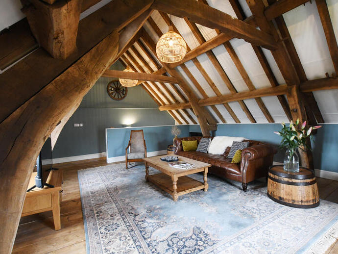 Lounge area at the top of a timber framed building, with exposed ceiling beams, a large leather sofa and wooden coffee table facing a flat-screen TV