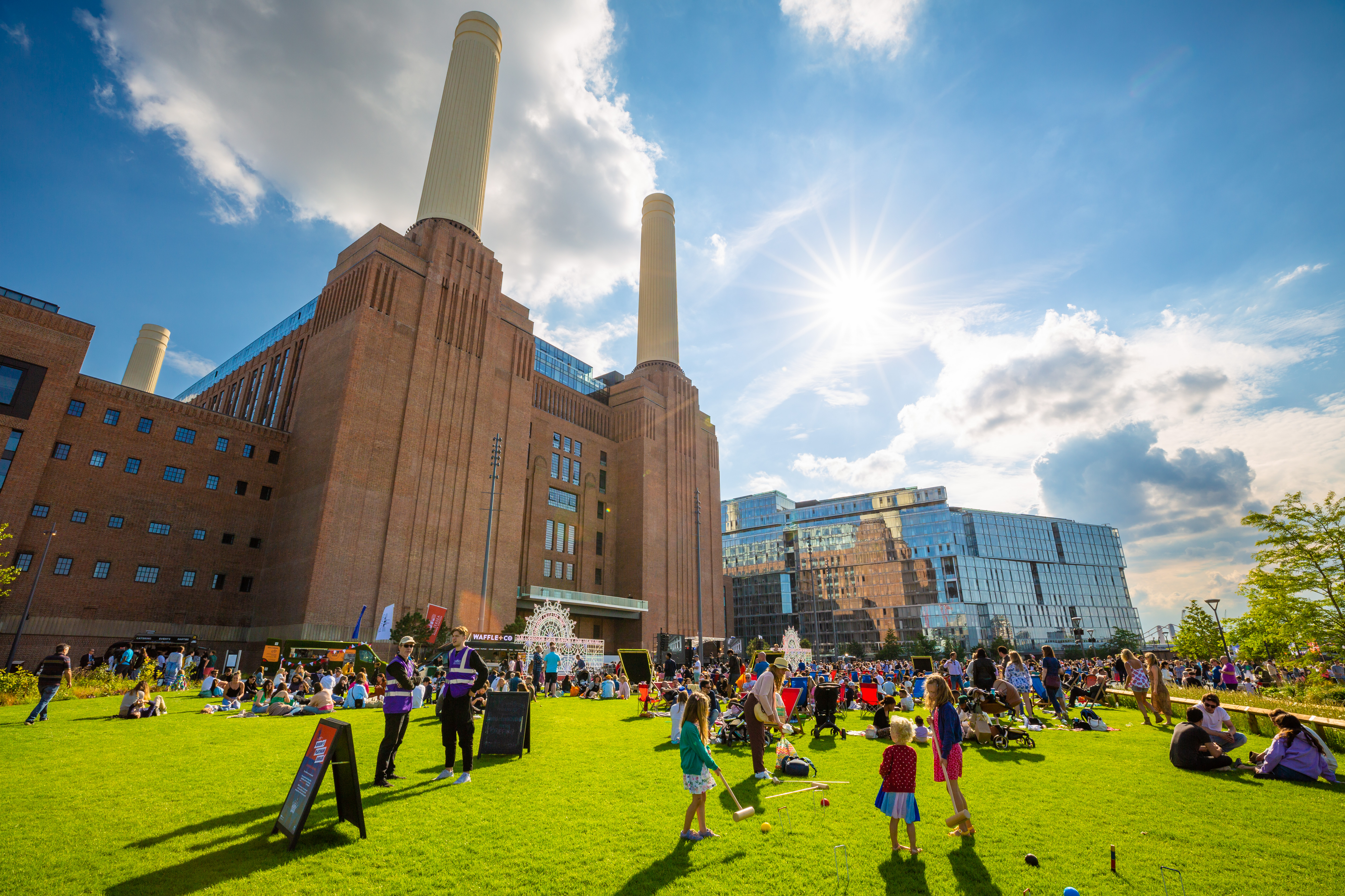 An outside shot of Battersea Power Station in the sun, surrounded by families and groups of people