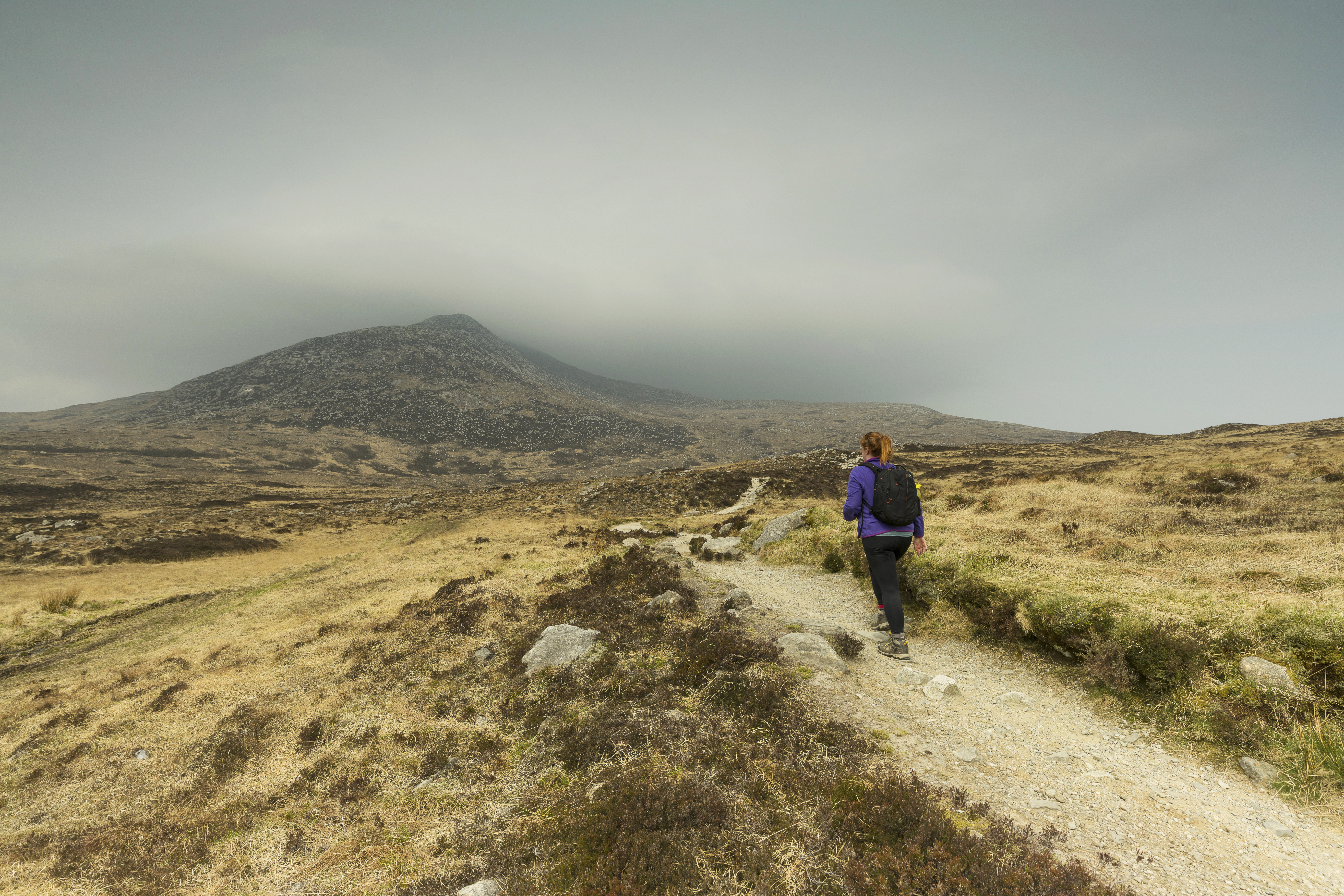 A girl walks on a path towards a mountain