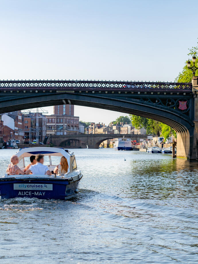 Small boat with four passengers cruising a river going under a bridge