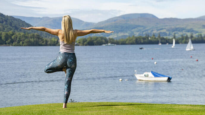 Une femme est debout dans une posture de yoga au bord d'un lac avec des montagnes en arrière-plan