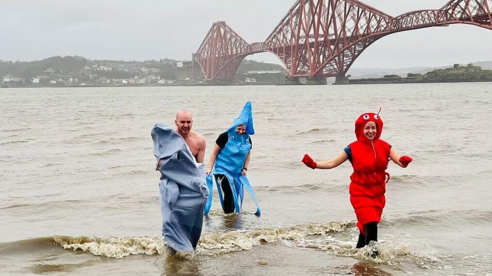 Eine Gruppe von Menschen in Tintenfischkostümen, die in South Queensferry aus dem Wasser auftauchen