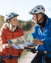 A man and a woman look at a trail map while riding e-bikes through a forest bicycle forest path.