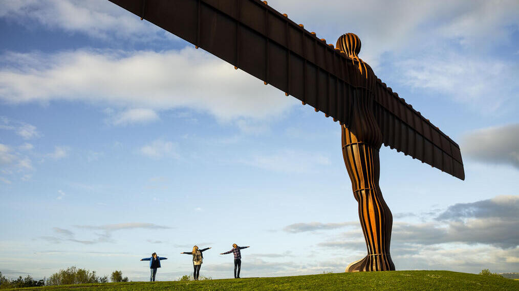 Three people posing near a giant steel sculpture