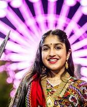 A woman celebrating Divali in front of a large lit up wheel