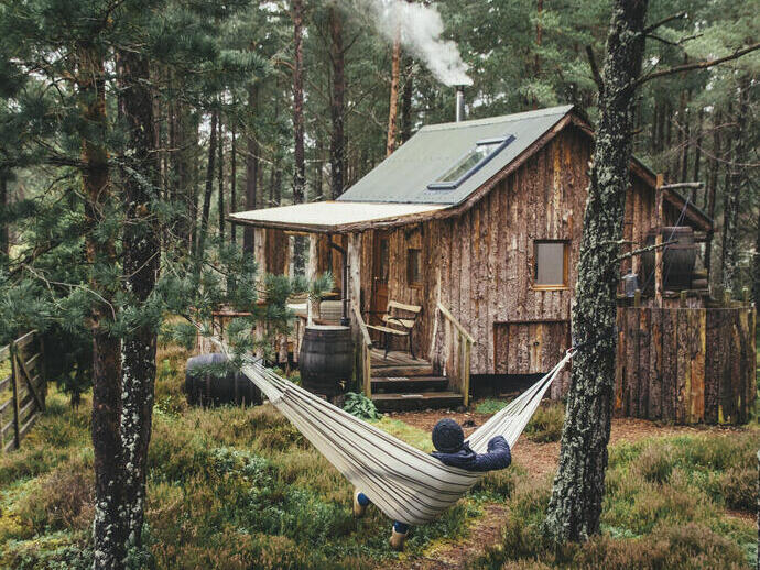 Man relaxing in a hammock outside a wooden cabin in a forest