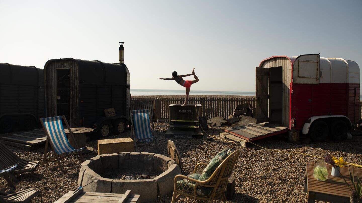 Woman holds a yoga pose standing on the edge of small plunge pool on the beach