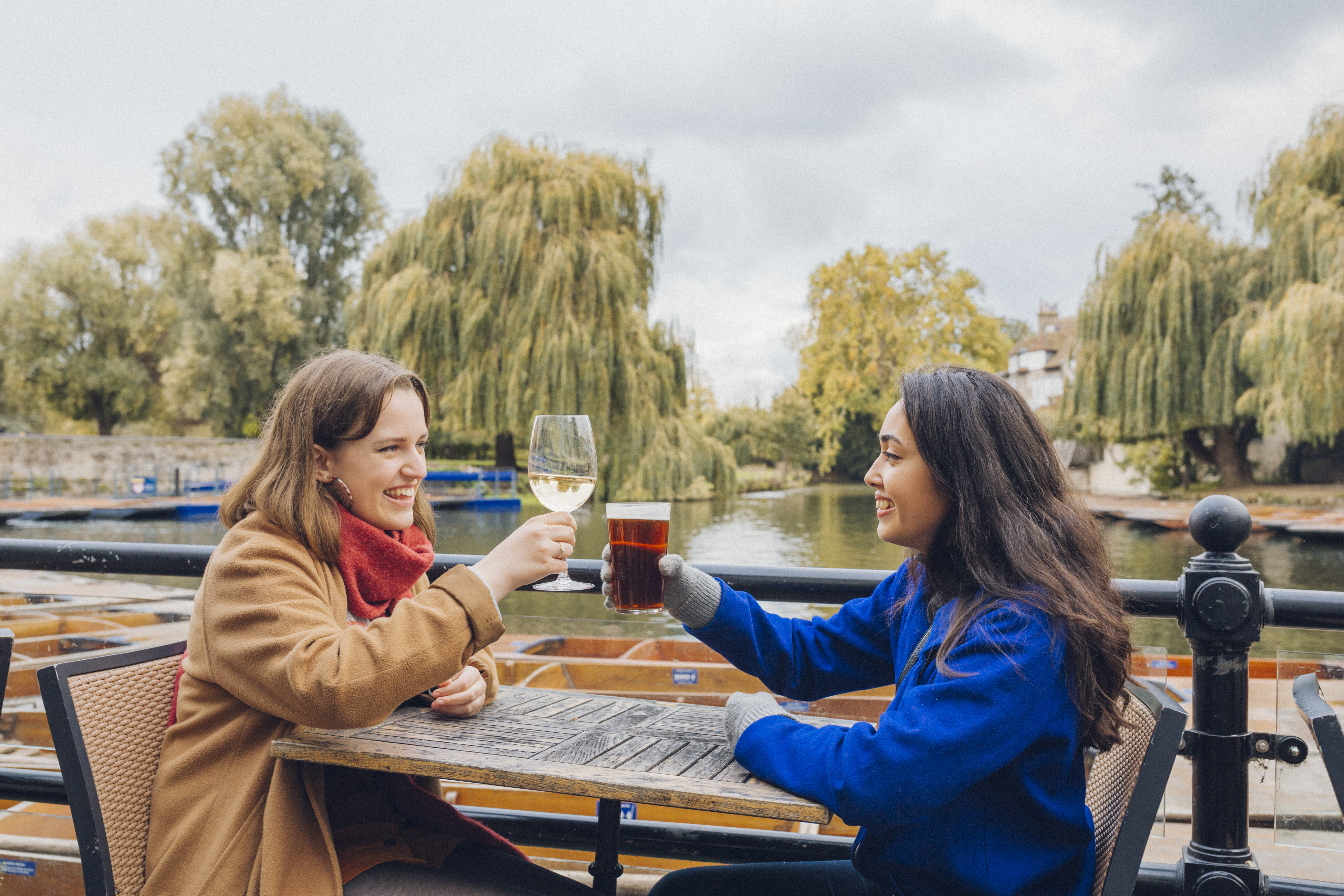 Two women toasting each other at a pub beside the river