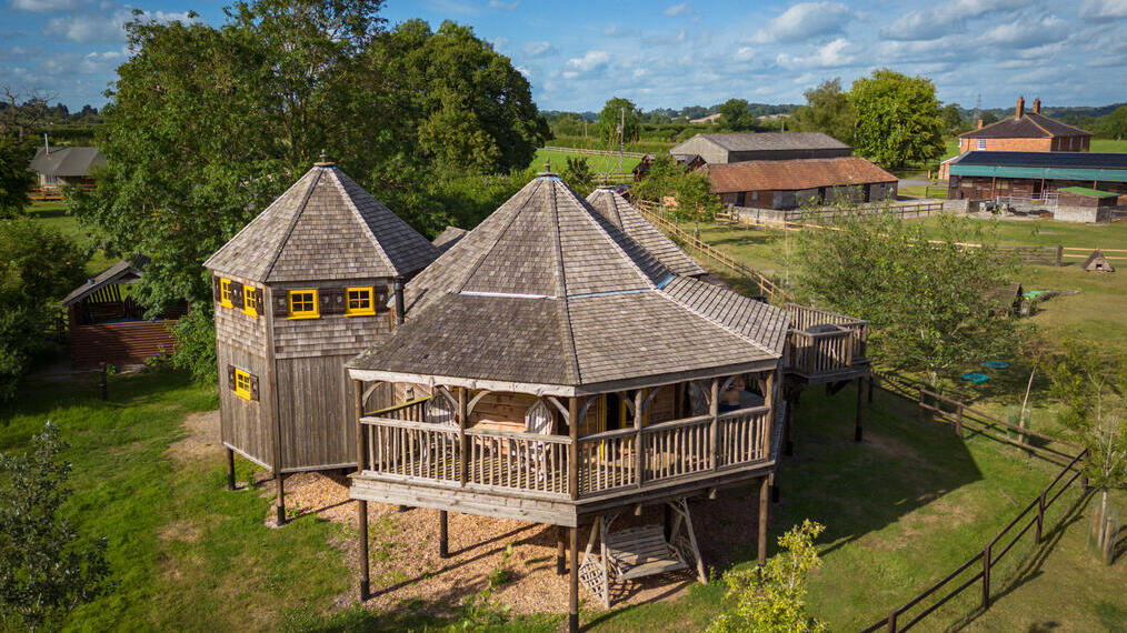 L'extérieur d'un grand hébergement de deux étages en bois, de style cabane dans les arbres, situé dans un champ.
