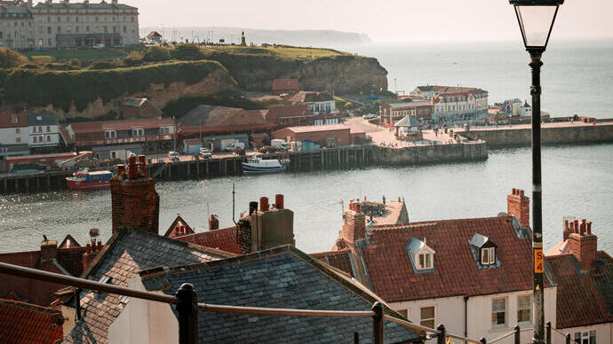 Looking down the steps at Whitby towards the sea with houses on the left side and the jetty and building on the outcrop in the distance