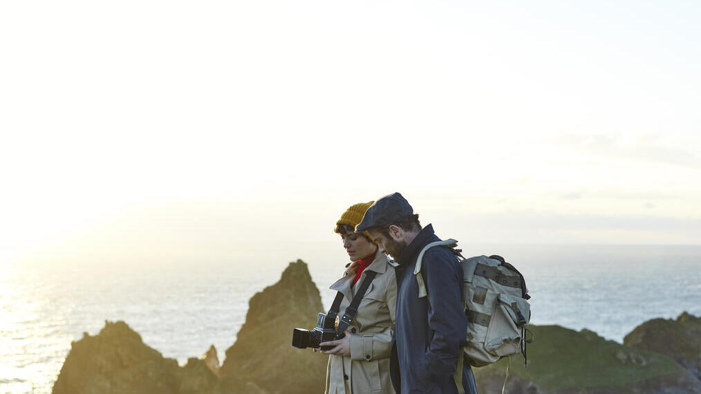 Couple debout au sommet des falaises, la femme tient un appareil photo et l'homme porte un sac à dos
