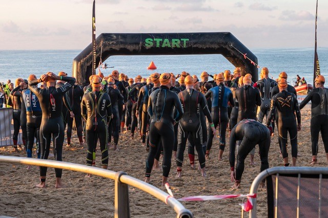 Competitors standing at the start line of a race wearing wetsuits.