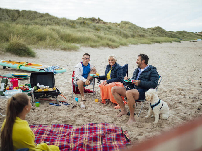 Une famille et leur chien assis à côté d'une couverture de pique-nique sur la plage