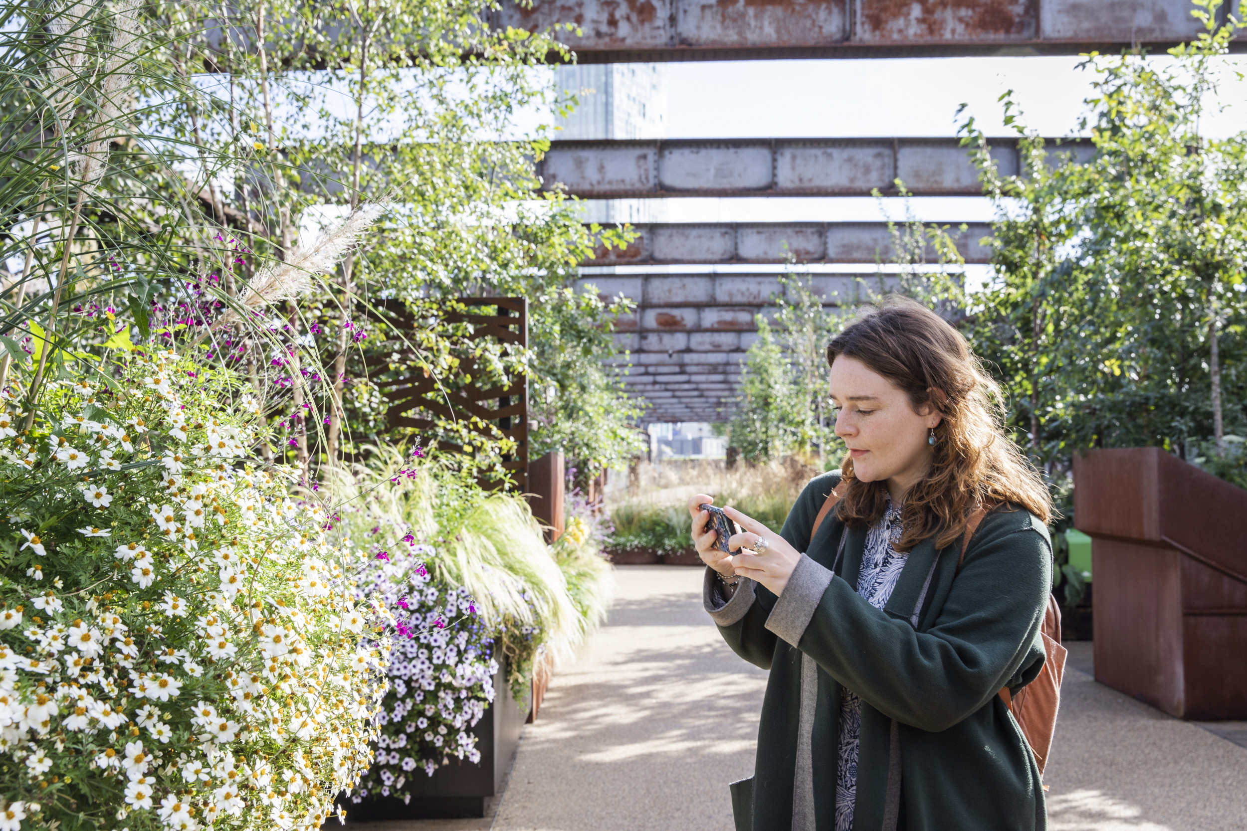 Une femme prenant une photo de plantes et de fleurs dans les jardins du viaduc de Castlefield, à Manchester