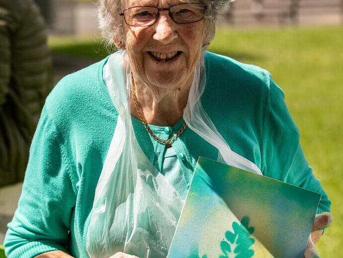 Mujer vestida de verde sosteniendo una obra de arte en una cafetería de la plaza