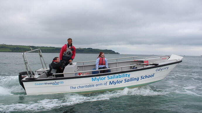 Man in a wheelchair steering a boat at sea accompanied by an instructor and woman