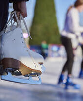 Hands holding a pair of white ice skates by the laces