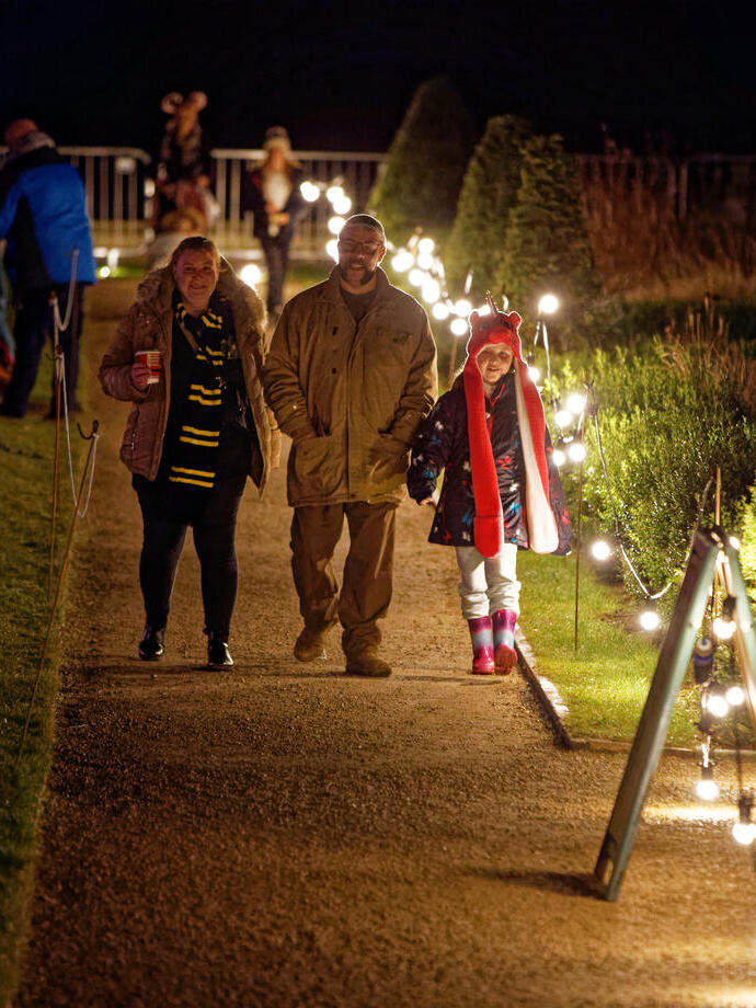 A family walking down a path lit up with fairy lights at night.