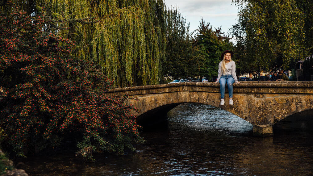 Woman sitting on low bridge over a river in a village